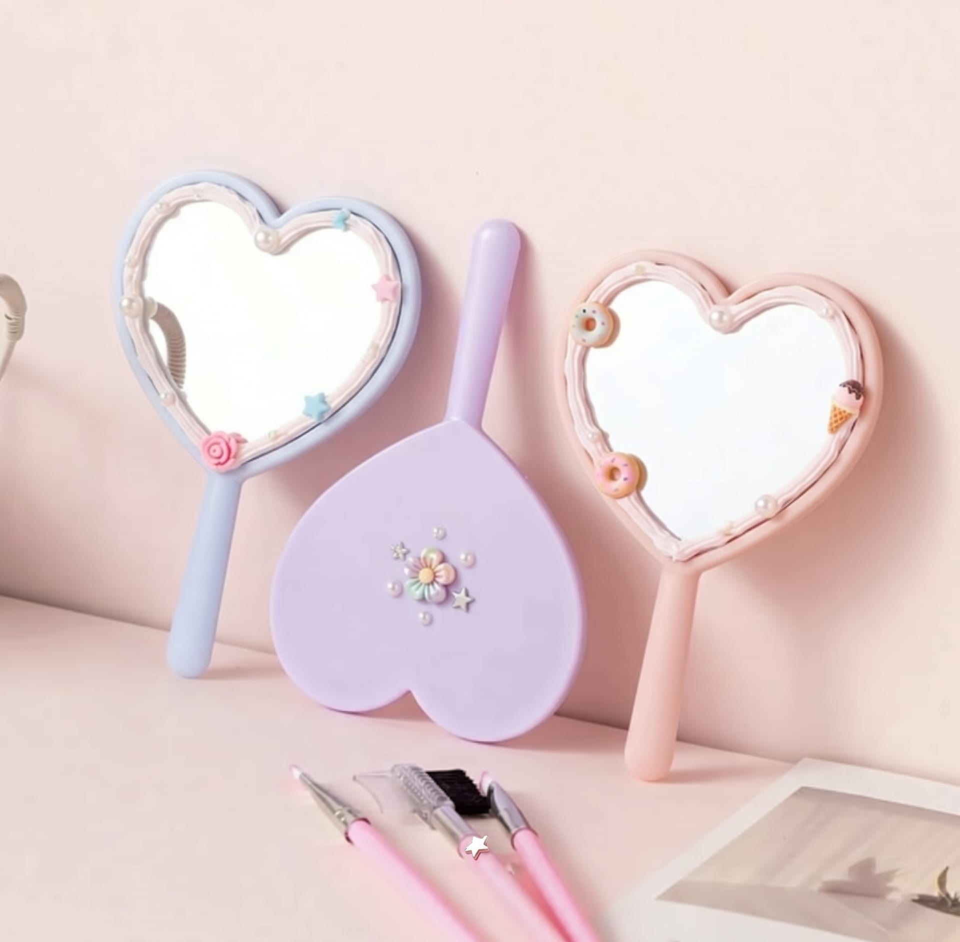 Three heart-shaped hand mirrors in blue, lilac and pink, trimmed with pearls, stars and tiny doughnuts