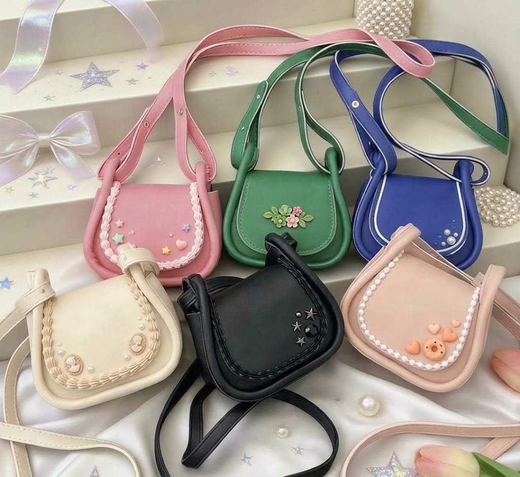 Six small crossbody bags in pink, green, blue, cream, black and blush, each with cream piping and charms